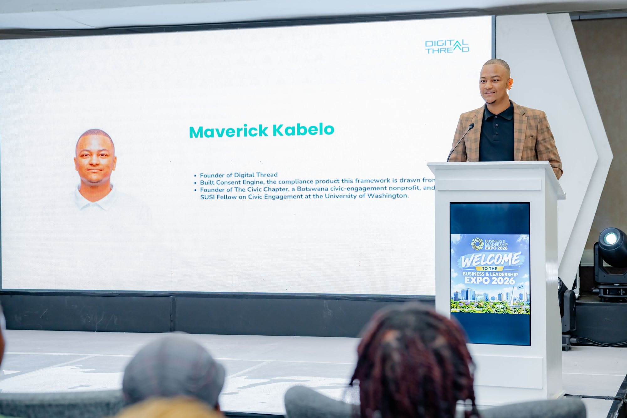 Maverick Kabelo at the lectern with his title slide on screen, listing Digital Thread, the Consent Engine and The Civic Chapter